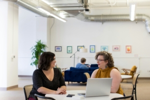 Two women in an office meeting. Human-centered design in change management offers a holistic approach that prioritizes the needs and experiences of the workforce.